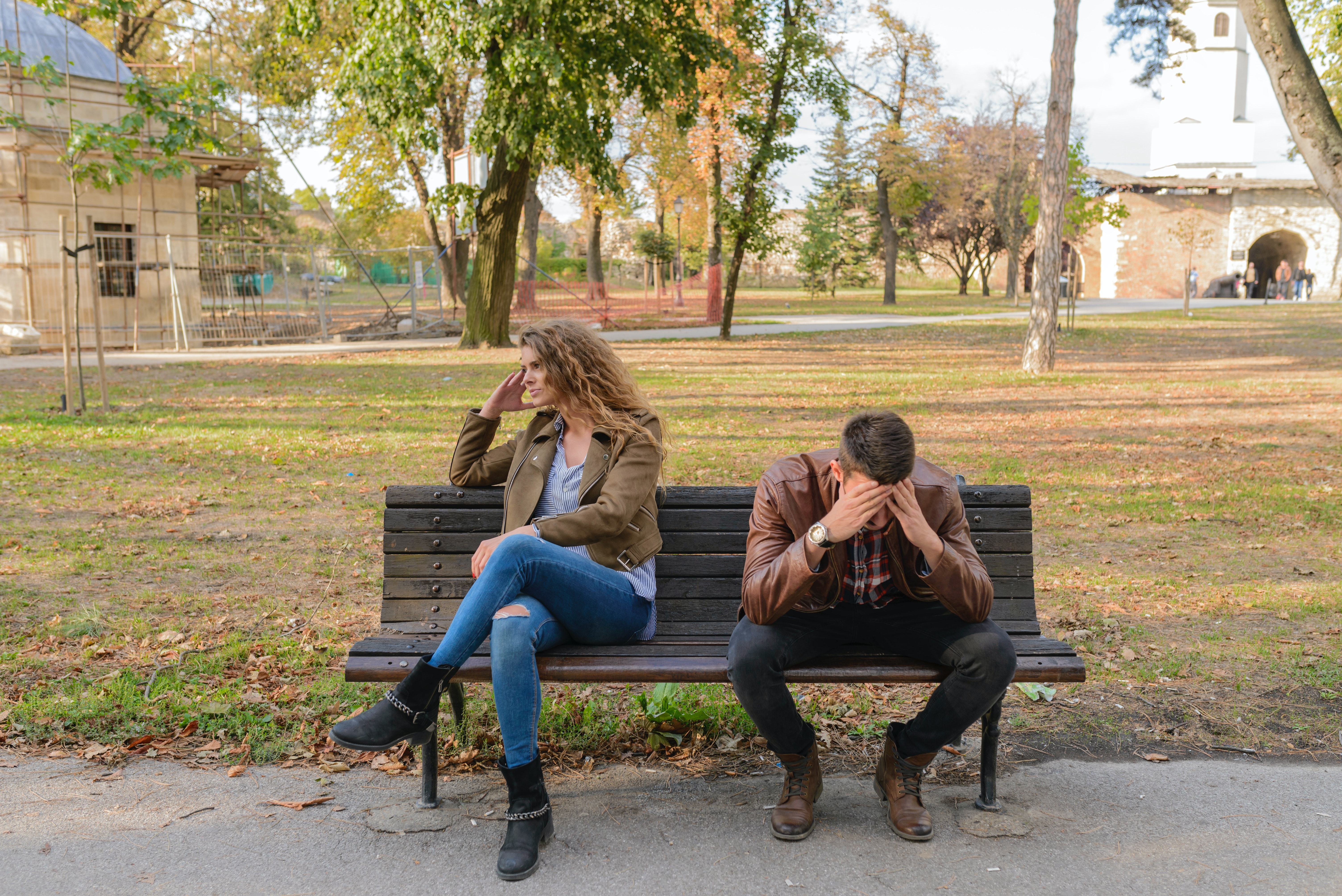 A couple fighting on a bench in a park